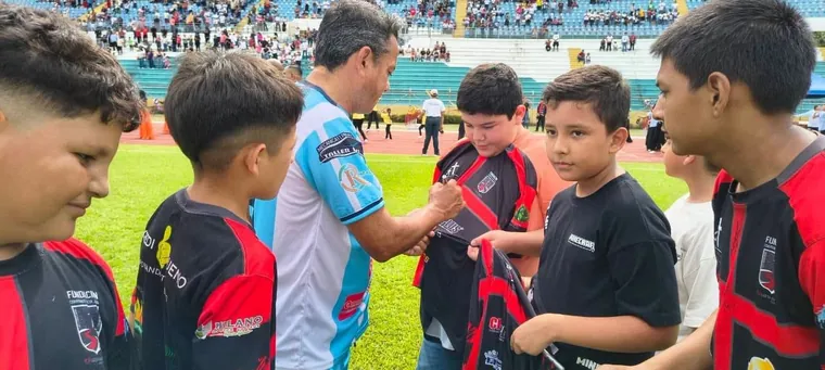 Niños reunidos junto a un futbolista que firma una camiseta