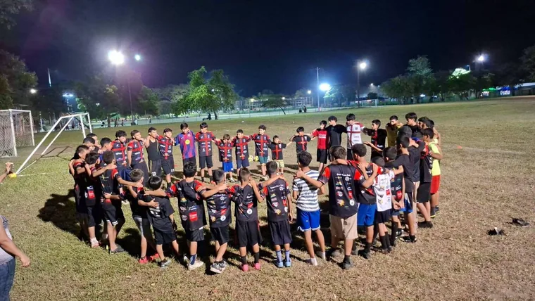 Grupo de niños y jóvenes formando un círculo de pie en la cancha