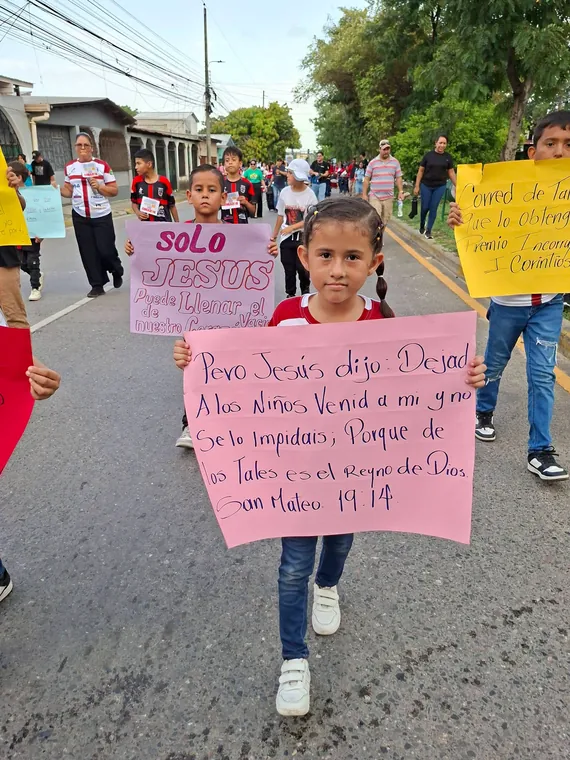Niña sosteniendo una pancarta con un mensaje de Jesús sobre la niñez